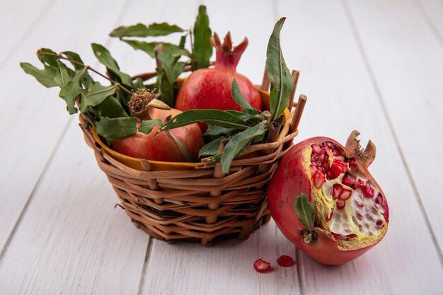 Front view pomegranates with branches of leaves in a basket on a white background