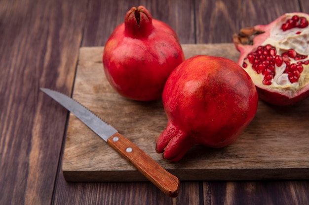 Front view pomegranates with a knife on a cutting board on a wooden wall