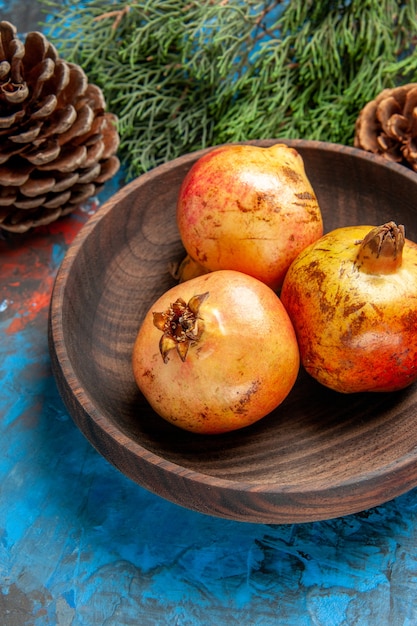 Front view pomegranates on wooden plate pine tree branch and cones on blue