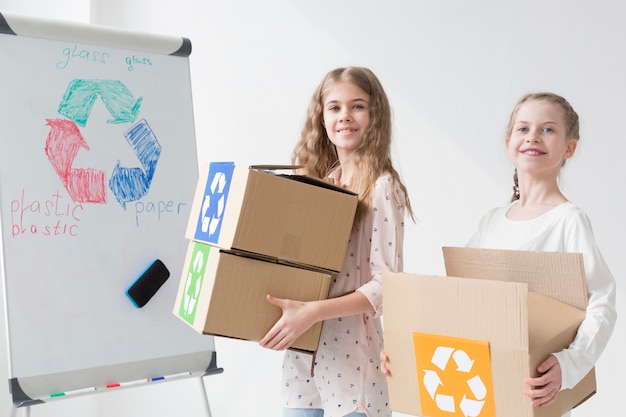 Front view positive young girls holding recycling boxes