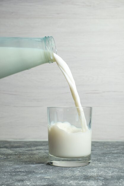 Вид спереди наливая молоко в маленький стакан на белом, пить молочный продукт молочный продукт