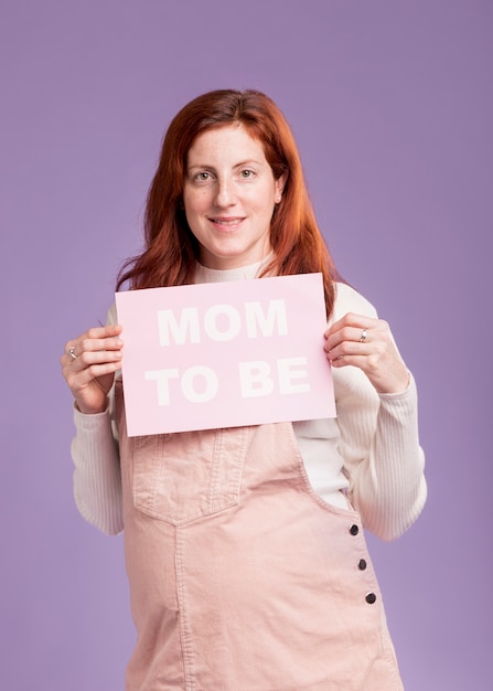 Free photo front view pregnant woman holding paper with mom to be message