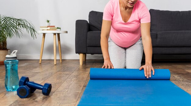 Front view of pregnant woman rolling up exercising mat at home