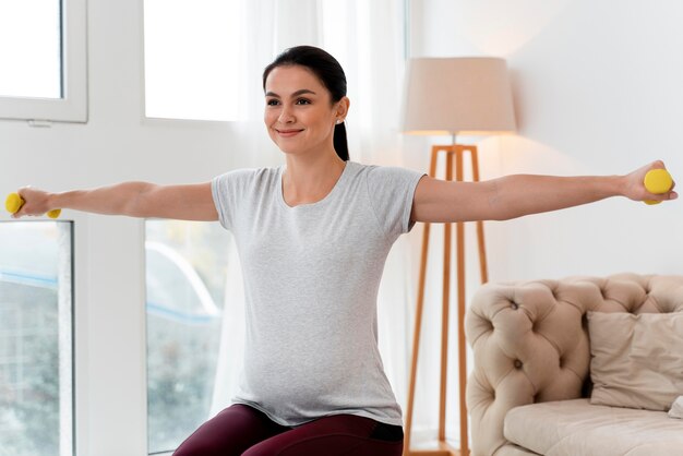 Front view pregnant woman using yellow weights