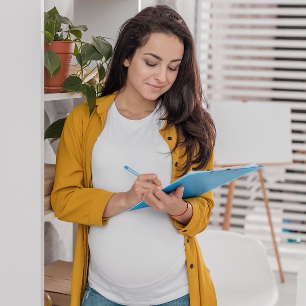 Foto gratuita vista frontale della donna incinta con appunti e matita