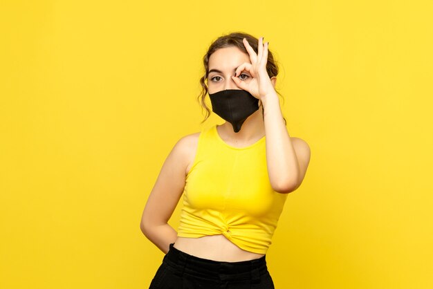 Front view of pretty female in black mask on yellow