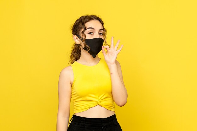 Front view of pretty female in black mask on yellow