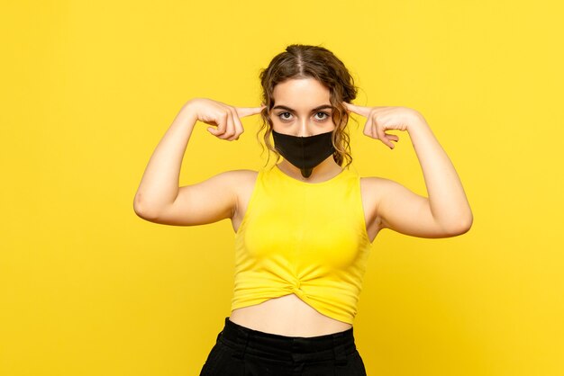 Front view of pretty female in black mask on yellow