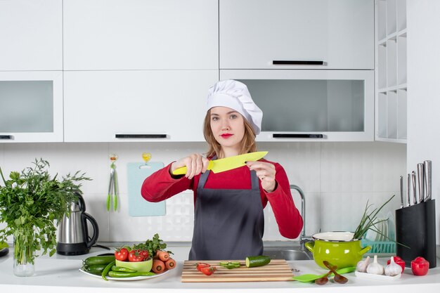 Вид спереди симпатичная женщина-повар в фартуке, подняв нож