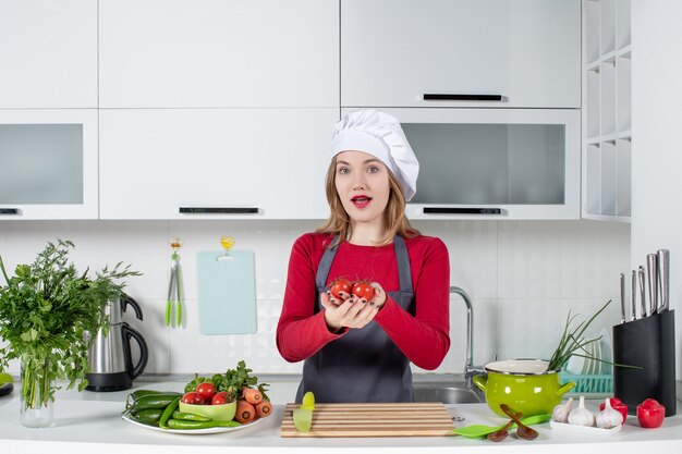 Front view pretty female cook in apron holding up tomatoes