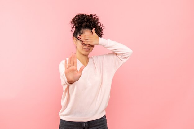 Front view of pretty female covering her face on pink