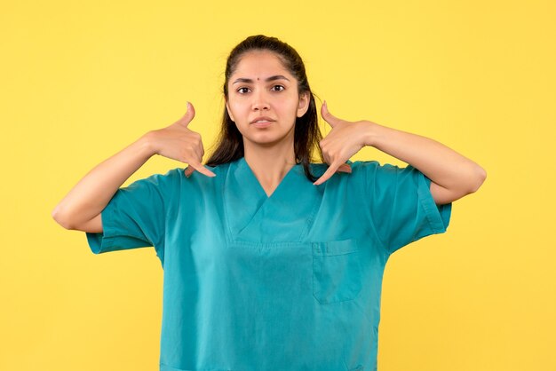 Front view of pretty female doctor making call me phone sign on yellow wall