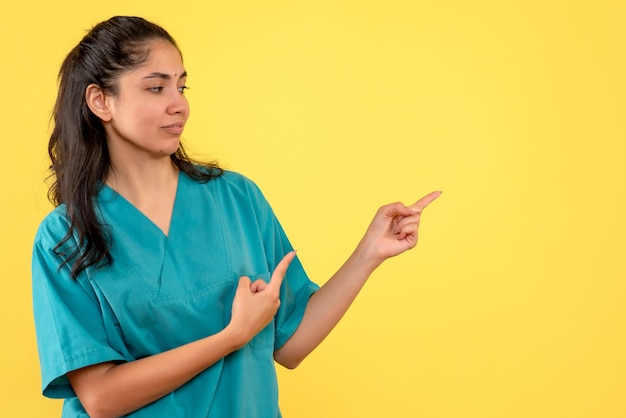 Front view of pretty female doctor pointing at right direction on yellow wall