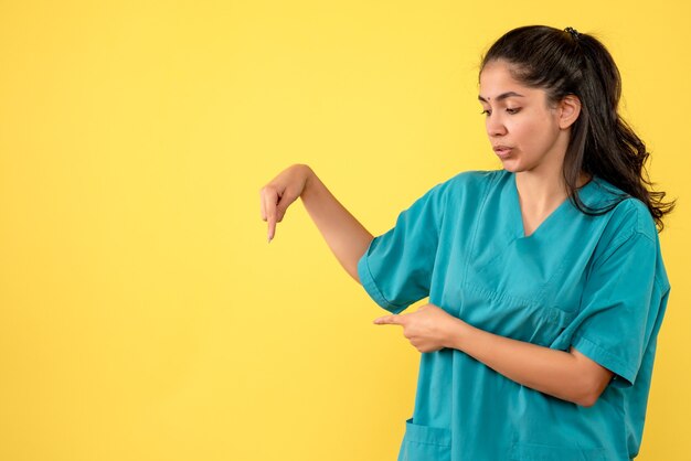 Front view of pretty female doctor pointing at wall. on yellow wall