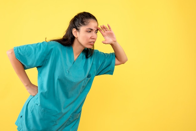 Vista frontale del medico femminile grazioso che mette la mano su una vita sulla parete gialla