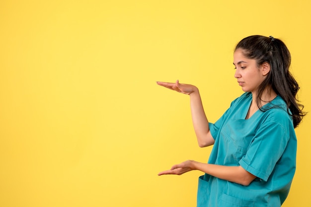 黄色の壁に手でサイズを示すきれいな女性医師の正面図