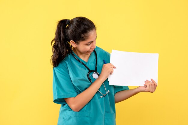 黄色の壁の文書を見て制服を着たきれいな女性医師の正面図