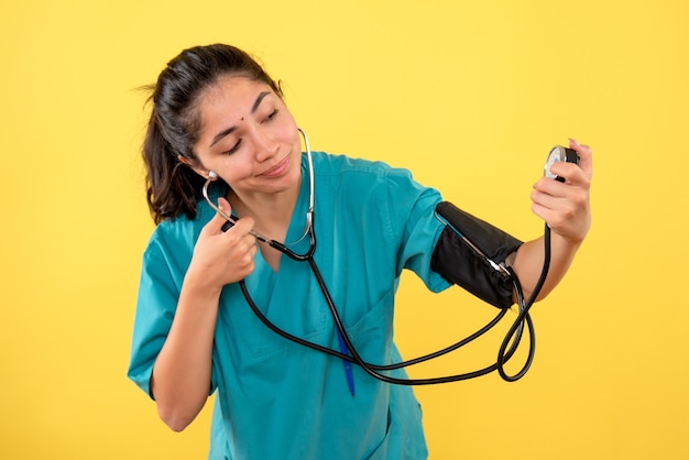 Free photo front view pretty female doctor in uniform using blood pressure measuring device on yellow background