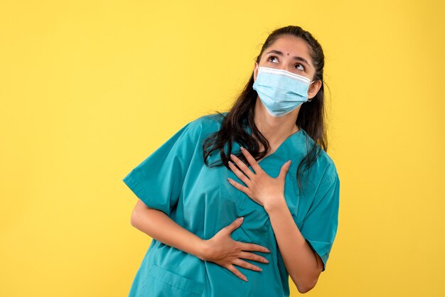 Front view of pretty female doctor with medical mask looking up on yellow wall