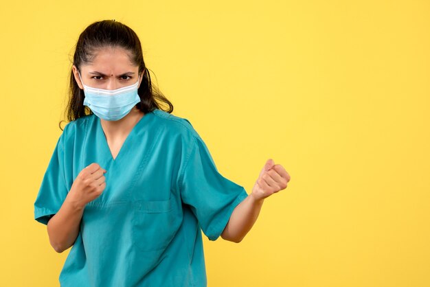 Foto gratuita vista frontale del medico femminile grazioso con mascherina medica che mostra i pugni sulla parete gialla