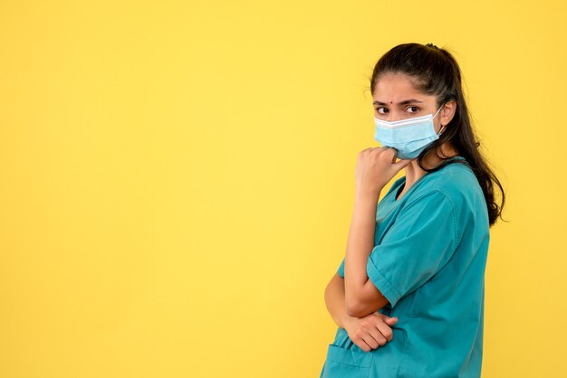Front view of pretty female doctor with medical mask on yellow wall