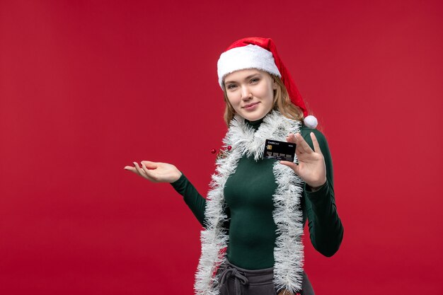 Front view pretty female holding black bank card on a red background