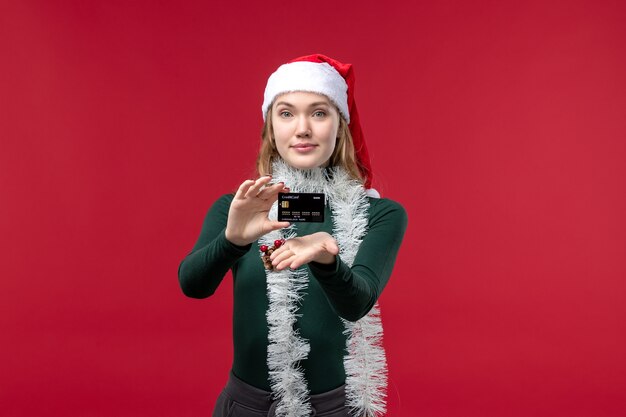 Front view pretty female holding black bank card on red background