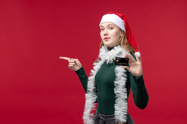 Front view pretty female holding black bank card on red background