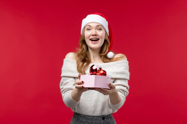 Front view of pretty female holding christmas toys on red