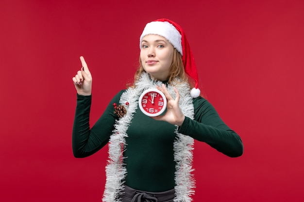 Front view pretty female holding clock on red background