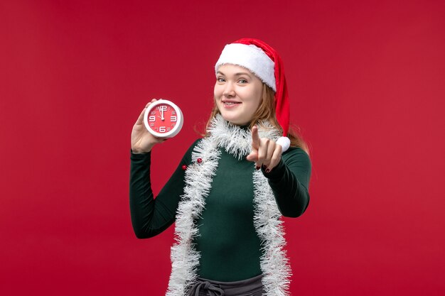 Front view pretty female holding clock on red desk