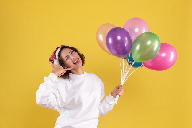 Front view pretty female holding colorful balloons on yellow 
