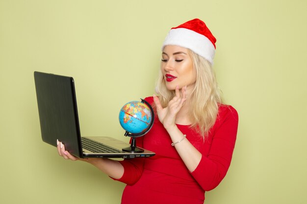 녹색 벽 크리스마스 색상 눈 휴가 새 해 감정에 작은 지구 글로브와 노트북을 들고 전면보기 예쁜 여성