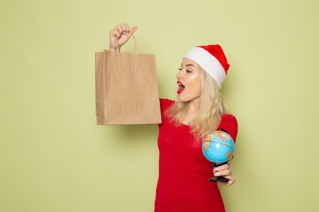 Front view pretty female holding little earth globe and package on green wall christmas color snow holiday new year emotion