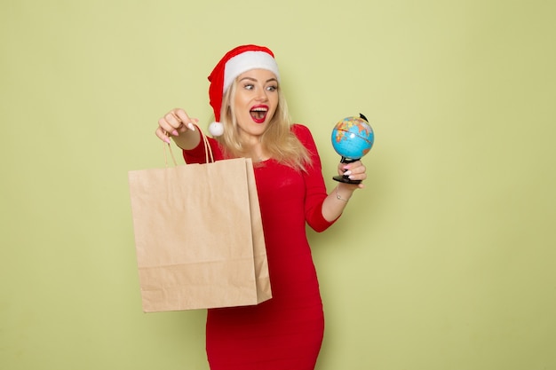 Front view pretty female holding little earth globe and package on a green wall color snow holiday christmas new year emotion