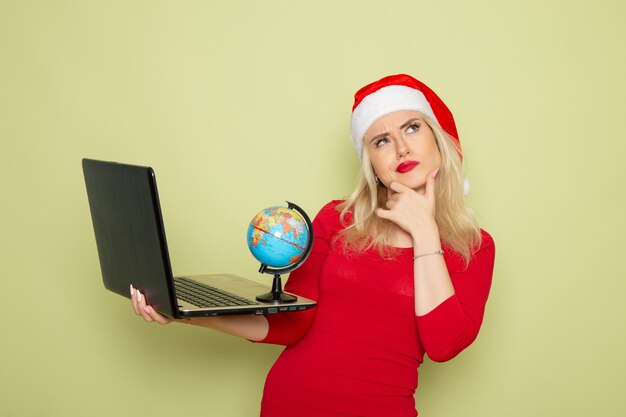 Front view pretty female holding little earth globe and using laptop on green wall christmas color snow holidays new year emotion