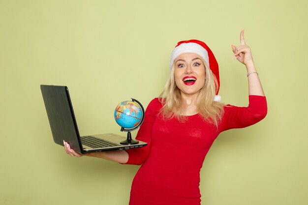 Front view pretty female holding little earth globe and using laptop on green wall christmas color snow new year emotion