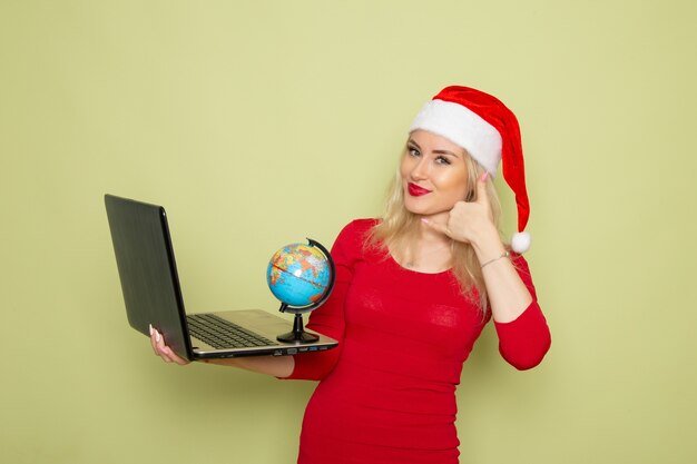 正面図きれいな女性が小さな地球儀を保持し、緑の壁にラップトップを使用してクリスマス雪の休日新年の感情