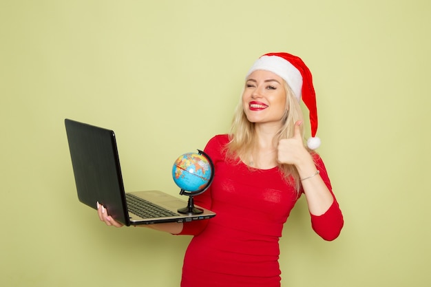 Front view pretty female holding little earth globe and using laptop on green wall color snow holiday new year emotion