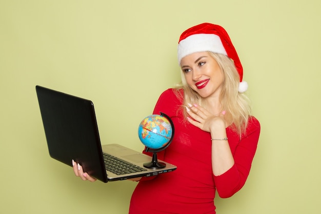 Front view pretty female holding little earth globe and using laptop on green wall holiday christmas snow color