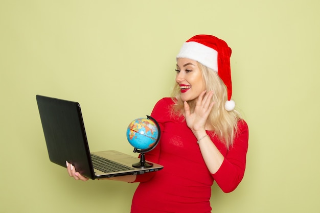 Front view pretty female holding little earth globe and using laptop on green wall holidays emotion christmas snow new year color