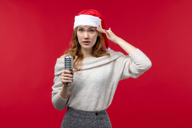 Front view of pretty female holding mic on red