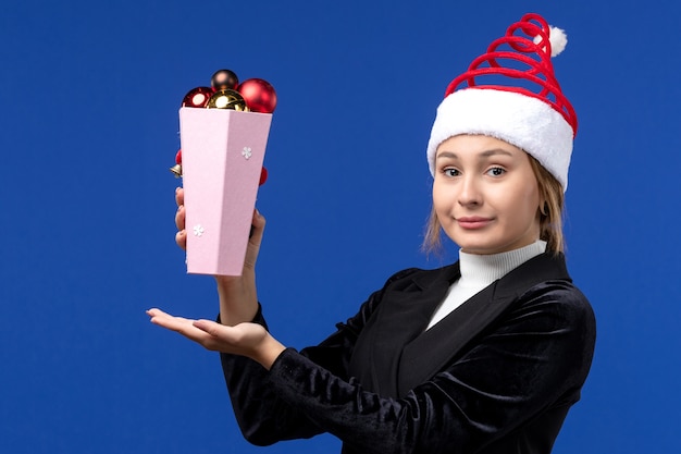 Vista frontale piuttosto femmina che tiene i giocattoli di plastica dell'albero sulla vacanza blu del nuovo anno della parete blu