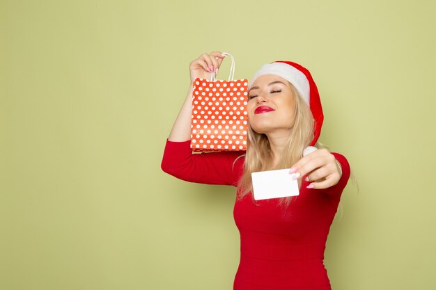 緑の壁の感情休日クリスマス色新年の小さなパッケージと銀行カードでプレゼントを保持している正面図きれいな女性