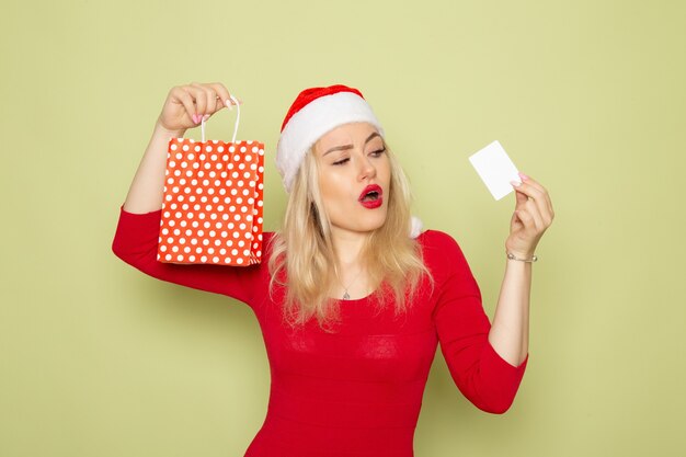 Front view pretty female holding present in little package and bank card on green wall emotions holiday christmas snow color new year