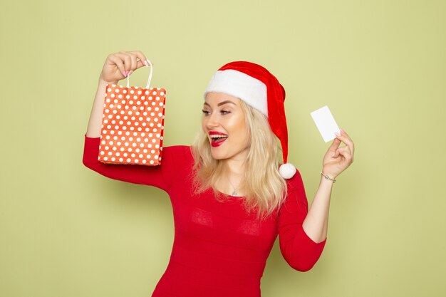 Front view pretty female holding present in little package and bank card on green wall snow emotion holiday christmas new year color