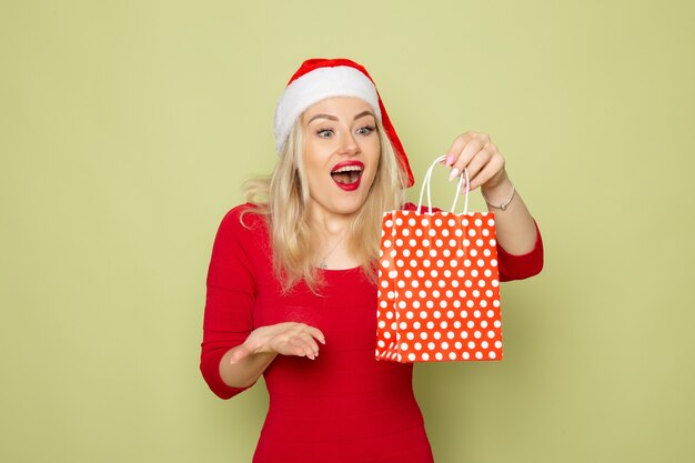 Front view pretty female holding present in little package on green wall holiday christmas color new year emotion