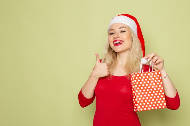 Front view pretty female holding present in little package on green wall holiday christmas snow color new year emotions