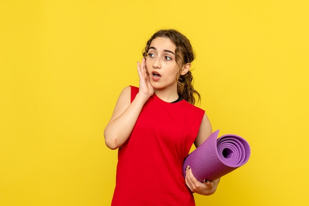 Vista frontale della femmina graziosa che tiene tappeto viola su giallo