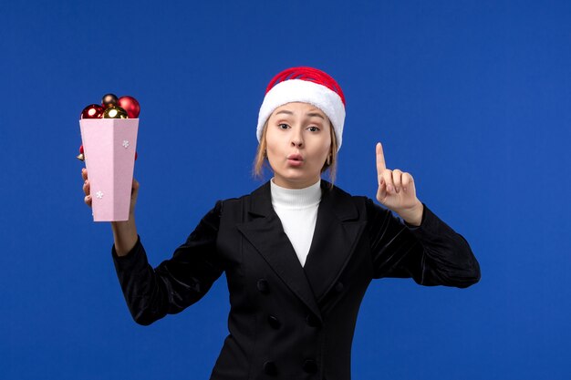 front view pretty female holding tree toys on a blue wall new year blue holiday woman
